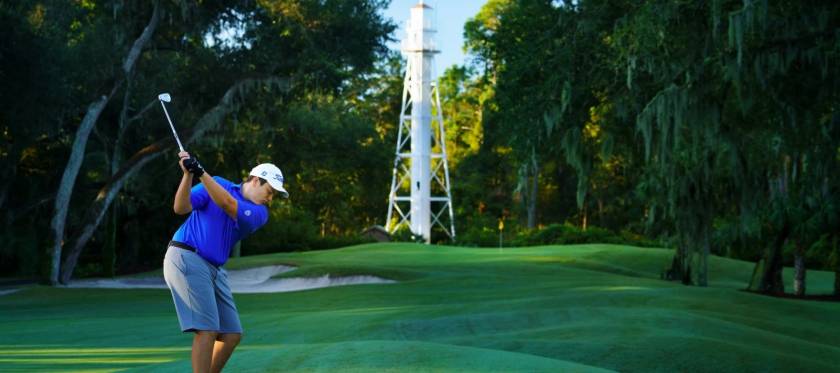 Male golfer mid swing at Arthur Hills Golf Course in front of the lighthouse